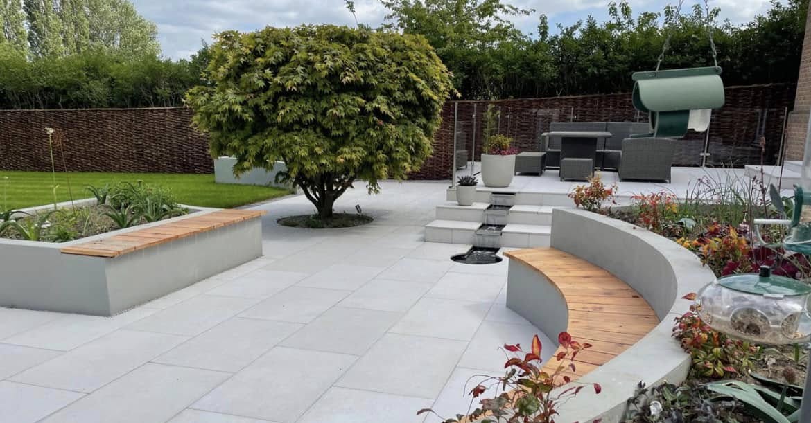 Designer garden with curved seating walls, water feature and tiered porcelain patio by Glorious Gardens Son & Co.